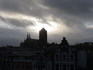 Silhouette of buildings, including one that has the appearance of a Christian church, are visible against the sun breaking through clouds.