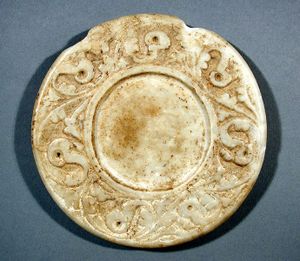 A circular stone of a pale hue, resembling a plate with a plain center and ornamented outer part.
