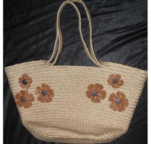 An uncolored bag made from jute fiber, with two handles and a simple floral pattern, using similar hues as the natural jute fiber color